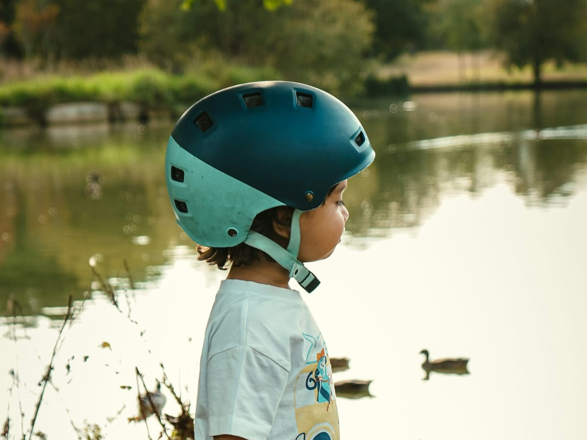 Kleines Kind mit Fahrradhelm am Ufer eines Sees