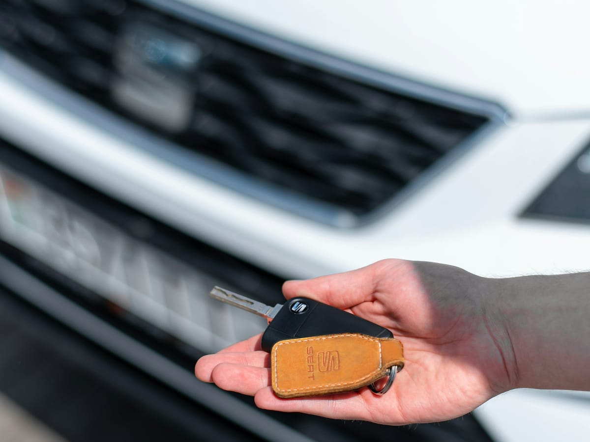 Hand holding a car key in front of a car at a dealership