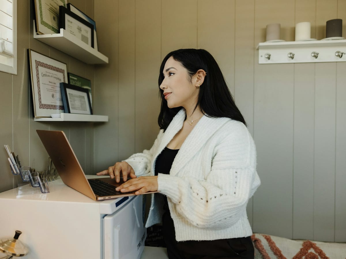 Woman answering customer messages on a laptop in a small office in the morning