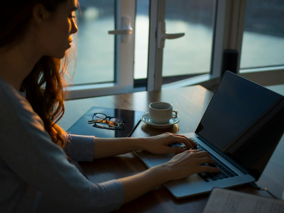Woman researching on a laptop at a table by the window