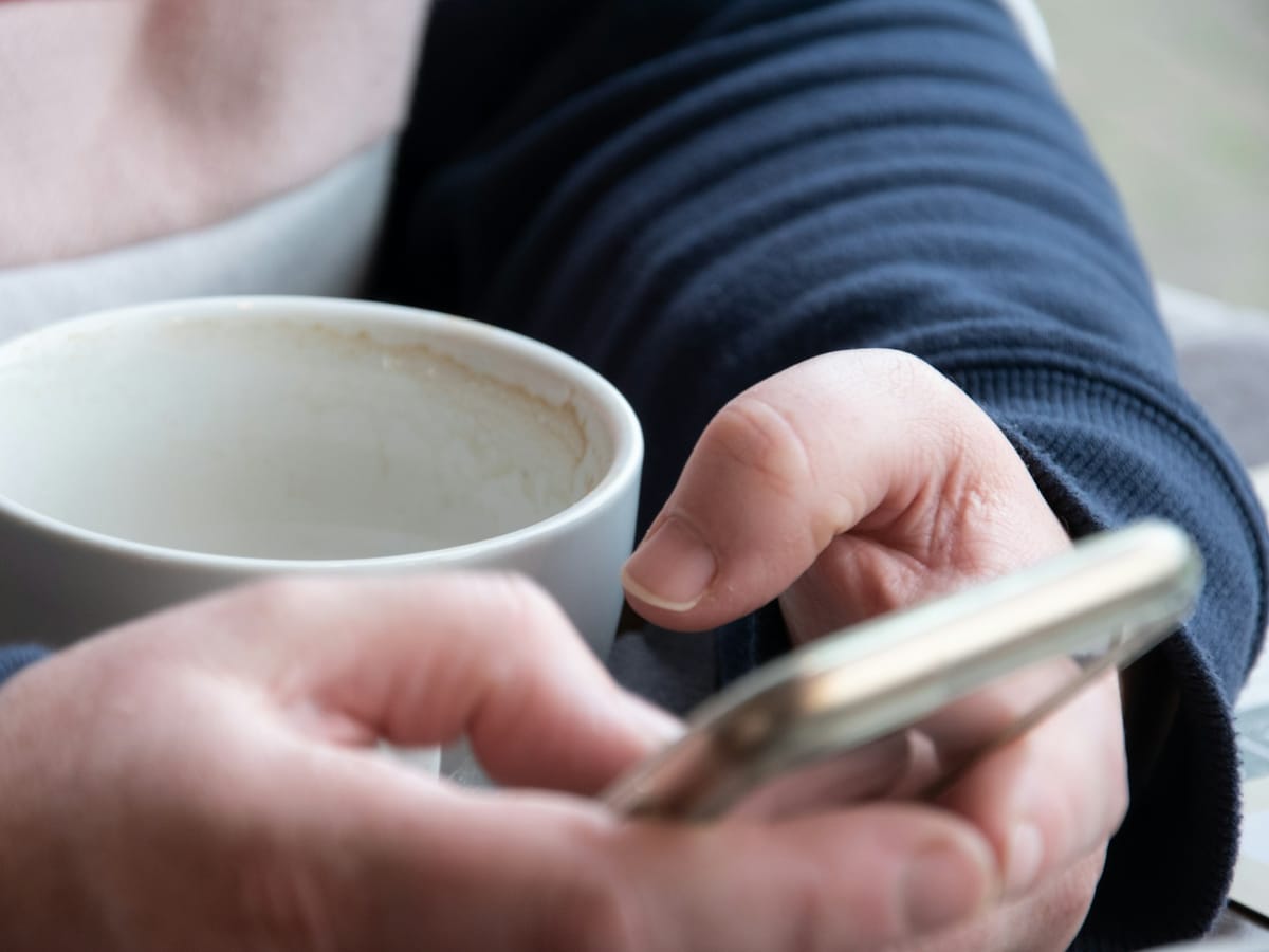 Hands typing on a smartphone next to a coffee cup